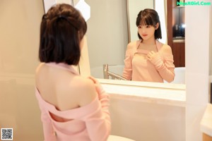 A woman in a pink sweater is standing in a bathtub.