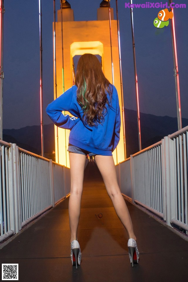 A woman in a blue sweatshirt and shorts standing on a bridge.
