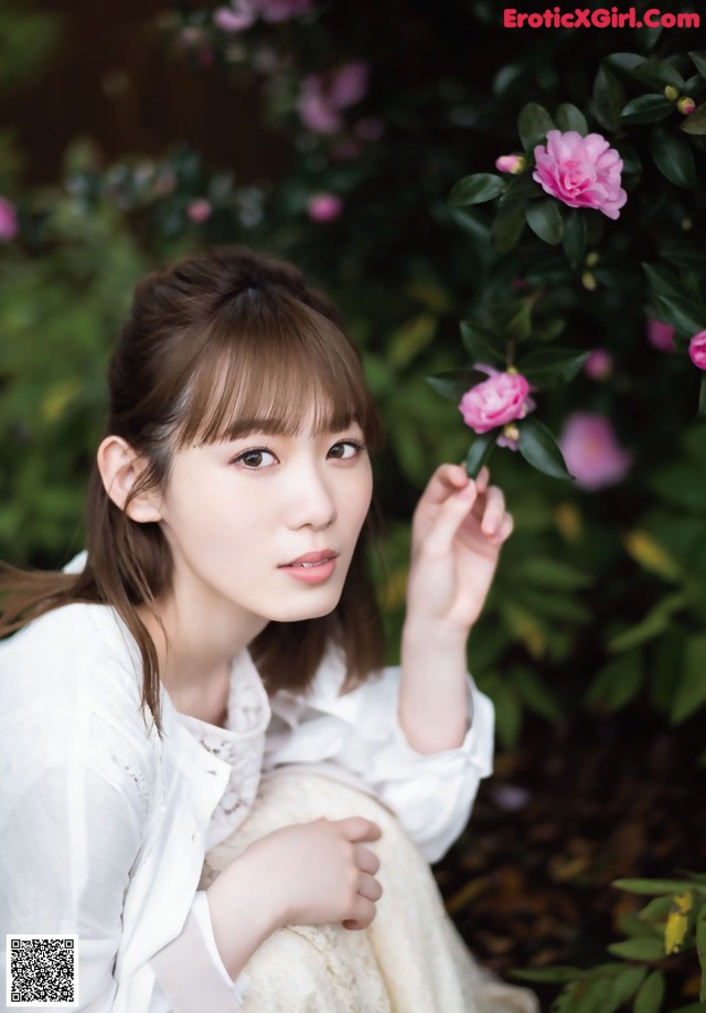 A woman in a white dress holding a pink flower.