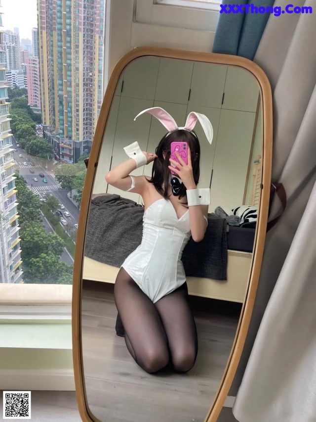 A woman in bunny ears taking a selfie in a mirror.