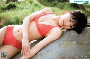 A woman in a bikini sitting on a rock by a river.