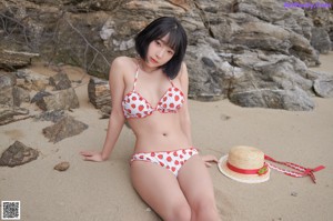 A woman in a bikini sitting on the sand.