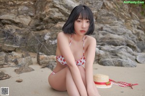 A woman in a bikini and a straw hat on a beach.