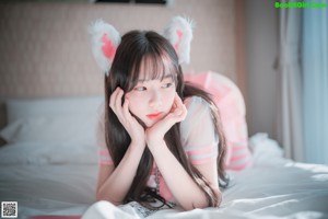 A woman in a pink and white outfit sitting on a bed.