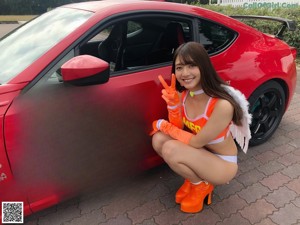 A woman in an orange and white outfit posing next to a red car.