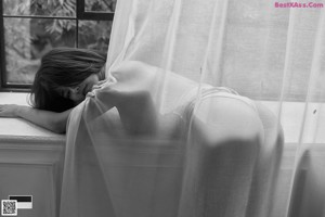 A black and white photo of a woman standing in front of a window.