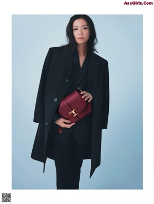 A woman in a black coat and black pants posing for a magazine.