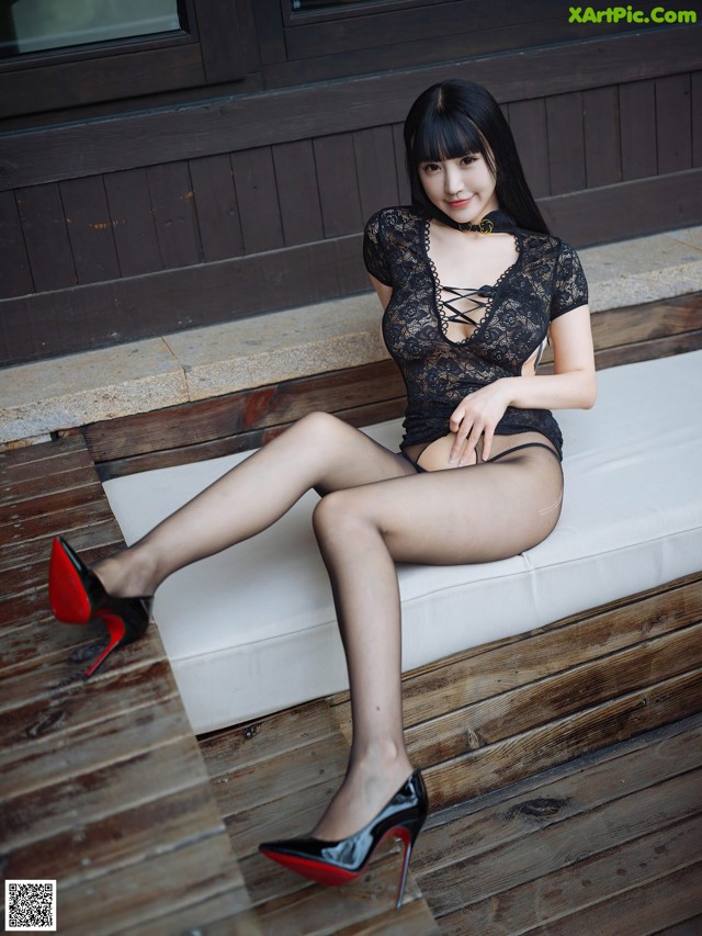 A woman sitting on a white bench wearing black stockings and high heels.