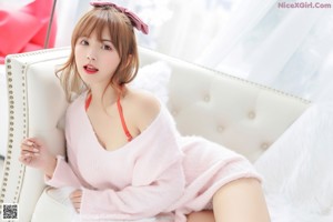 A woman in a pink sweater and panties sitting on a bed.
