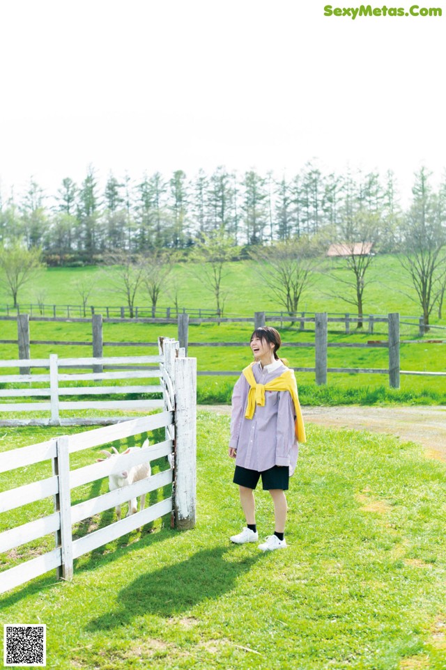 A woman standing in a field next to a white fence.