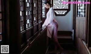 A woman in a gray dress sitting on a bed.