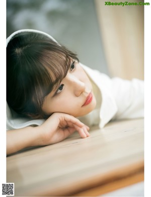 A woman in a white hooded robe sitting on a wooden bench.