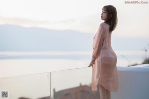 A woman in a pink dress standing on a balcony.