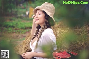 A woman sitting on a pile of hay next to watermelons.