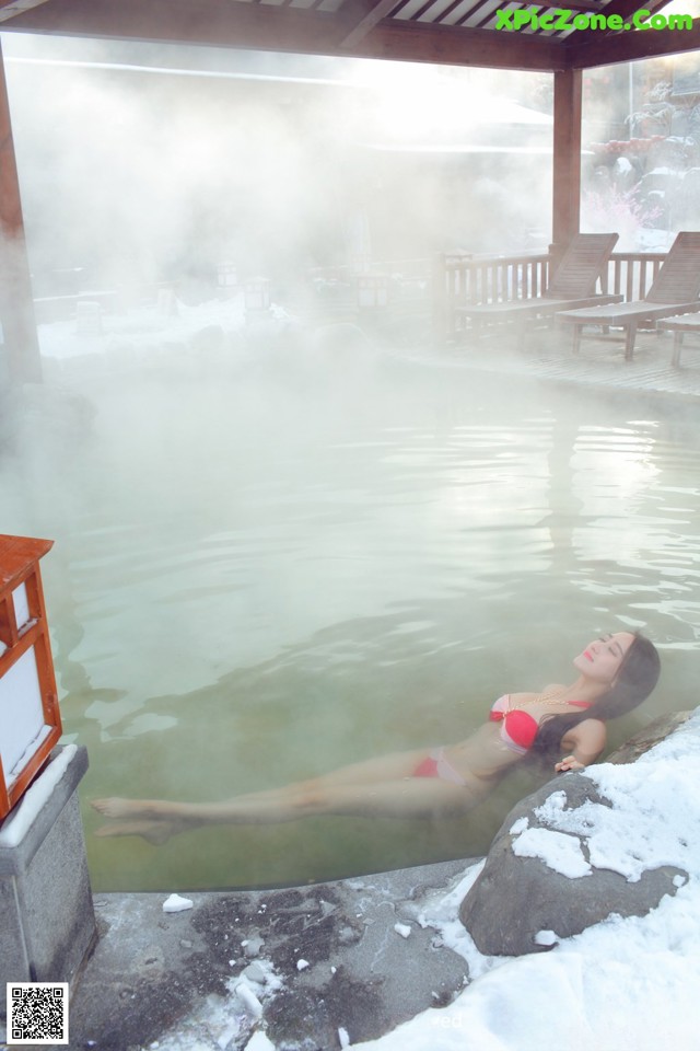 A woman in a red bikini laying in a hot spring.