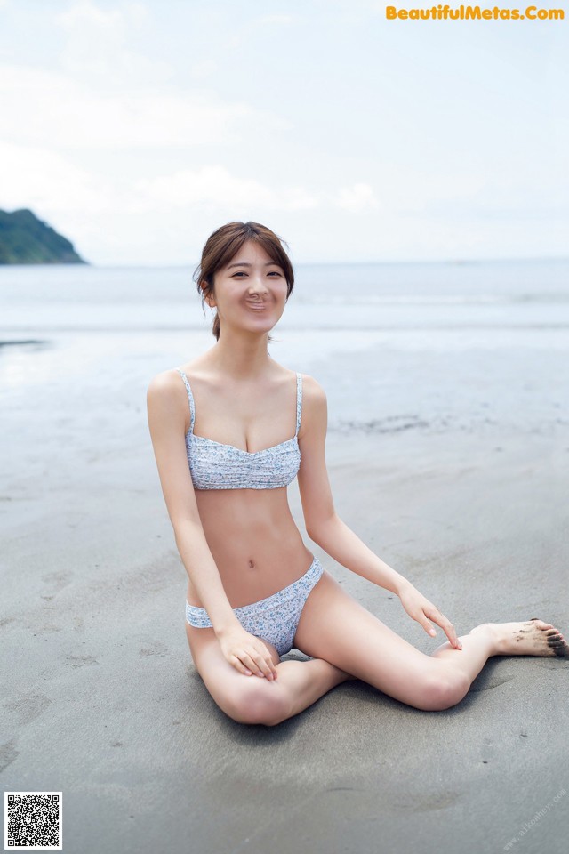 A woman in a bikini sitting on the beach.