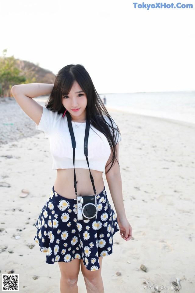 A woman standing on a beach holding a camera.