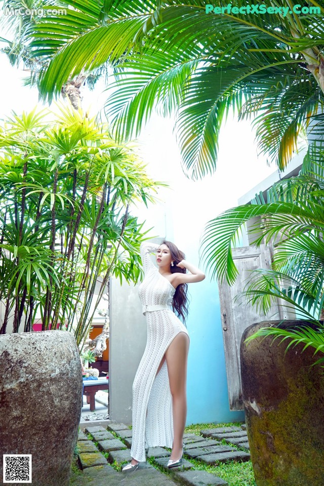 A woman in a white dress standing in front of a palm tree.